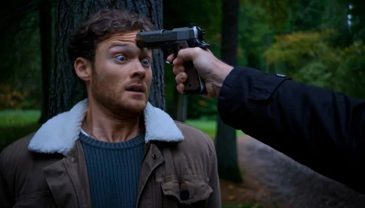 A young man against a tree, a pistol at his forehead