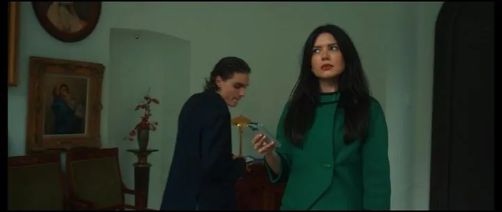 A woman in a green suit and a man with a phone in the manor salon