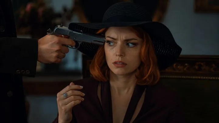 A woman in a hat, a pistol at her temple