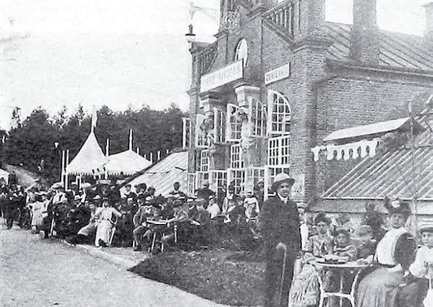 Riviera Cafe Crowds in Lentvaris Crowds seated at outdoor tables beside a brick pavilion with awnings and a marquee tent, early 1900s