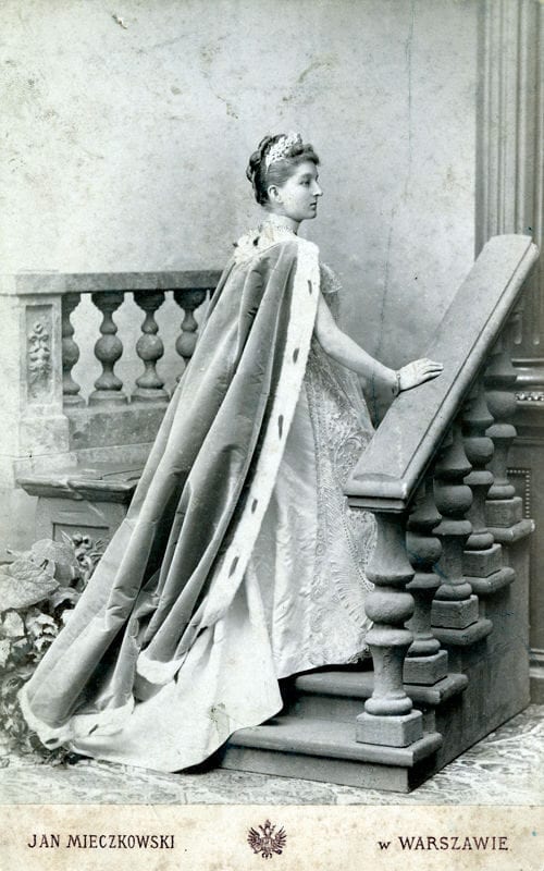 Studio portrait of an aristocratic woman in court gown, tiara and ermine-lined train on a staircase