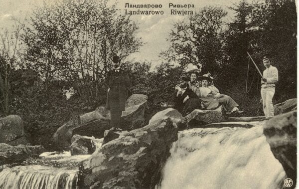 Vintage postcard of people in early 1900s dress posing on rocks beside a waterfall