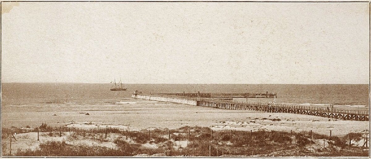 Historic Palanga Pier Photograph Sepia photograph of a long wooden pier stretching into the sea from a sandy dune shore, with a steamship offshore