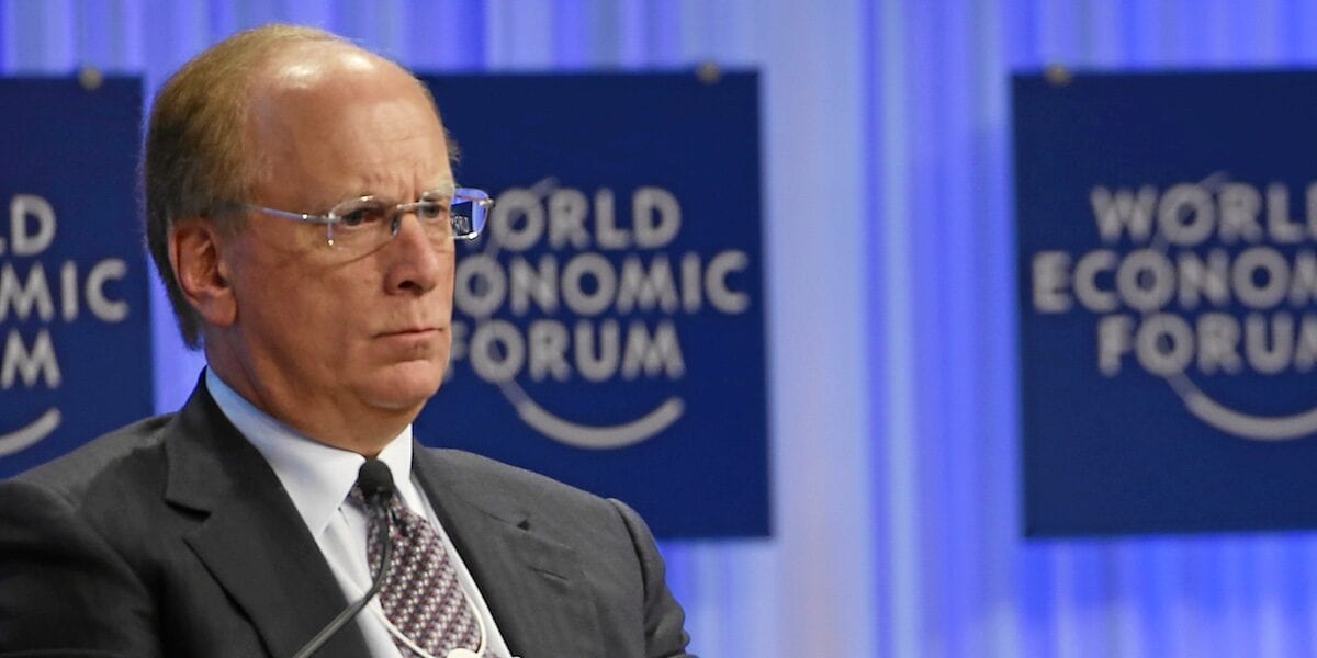 Asset Managers Back Tokenisation Executive in dark suit seated before World Economic Forum panel backdrop, looking off-camera